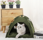 Cat inside a green tent-like pet bed with a wooden dresser and plants in the background.